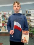 Uczniowie w bibliotece szkolnej, trzymają flagę Polski