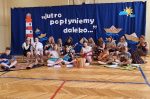 Dzieci siedzące na parkiecie sali gimnastycznej, grające na ukulele