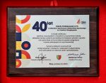 Tabliczka pamiątkowa z okazji 40-lecia SP-13 w Żorach - na drewnianym podłożu srebrna tabliczka z czarnym tekstem. Po lewej geometryczne kształty w kolorach czerwonym, granatowym, żółtym. W lewym górnym roku - duży napis "40 lat"