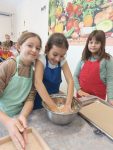 Dzieci ubrane w fartuchy wyrabiają ciasto rękami. W tle pozostali uczniowie.